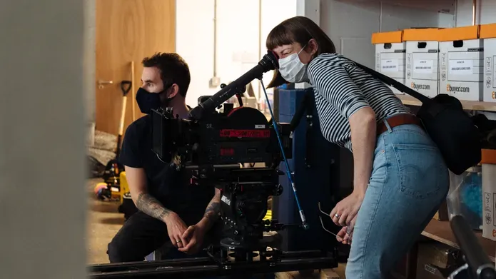 Rose Hendry, wearing a face mask, operates a film camera on tracks.