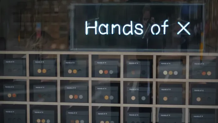 a rack of pigeonholes containing boxes with coloured dots on them, and the title 'hands of x' above