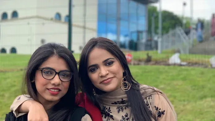 Falak and Suman standing on grass in front of a building with lots of glass