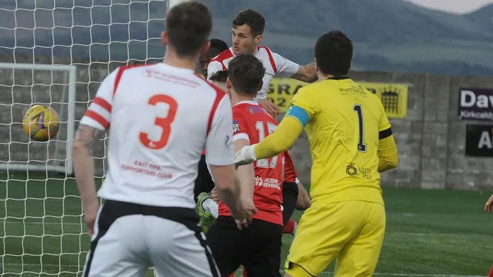 4 men playing football and goalposts in the background