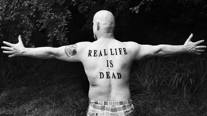 naked man with outstretched arms and tattoo of 'real life is dead'