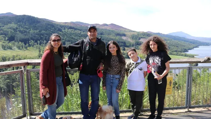 a family of 5 people with hills and a fence behind them