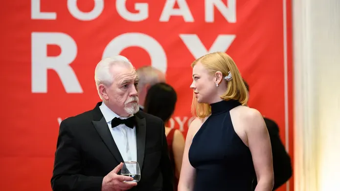 Brian Cox on the set of Succession with a banner in the background in big text of his characters name, Logan Roy