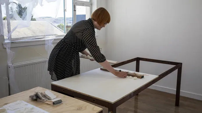 Mhairi Wilde in a studio setting leaning over a table and placing objects in a line