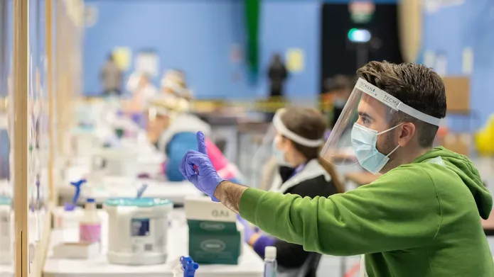 A man sitting in a Covid testing centre holding a syringe
