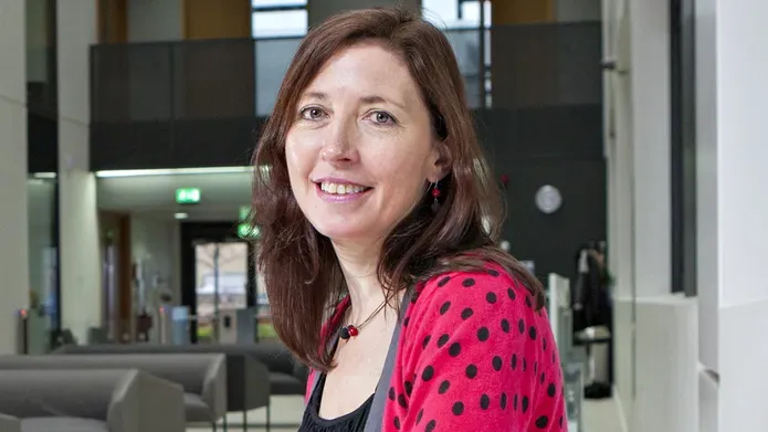 woman sitting in area with sofas, wearing a bright red cardigan with black spots