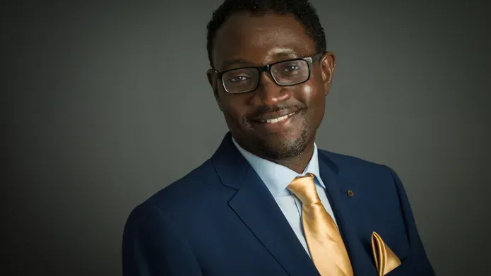 middle-aged black man wearing dark navy suit jacket and light yellow silk tie, wearing glasses
