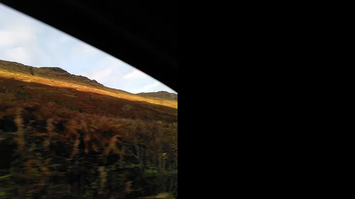 A window frame with a view of a sunlit hill and blue sky