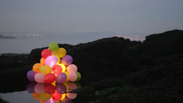 Colourful balloons in the foreground and dark landscape behind