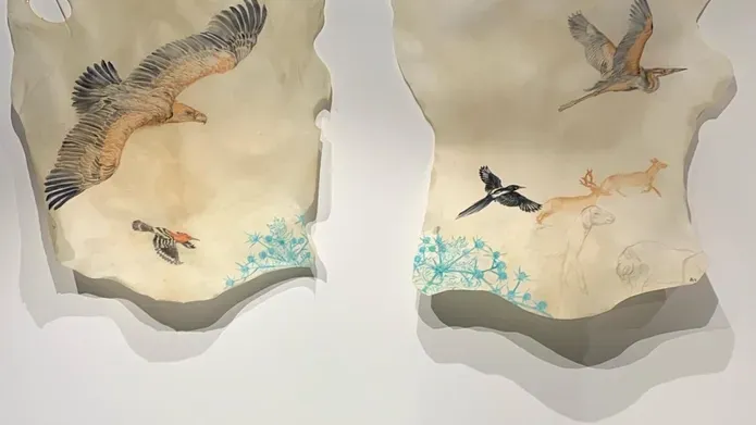 two roughly cut pieces of light fabric with flying birds drawn on them, hanging on white wall