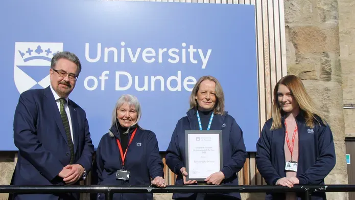 a middle aged man standing by two middle aged woman, one holding a framed award, who stand next to a young girl in her 20's