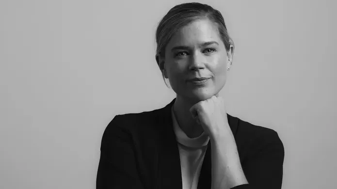 Sheryl Bartlett poses with hand under chin wearing black jacket against a plain background, in grayscale image.
