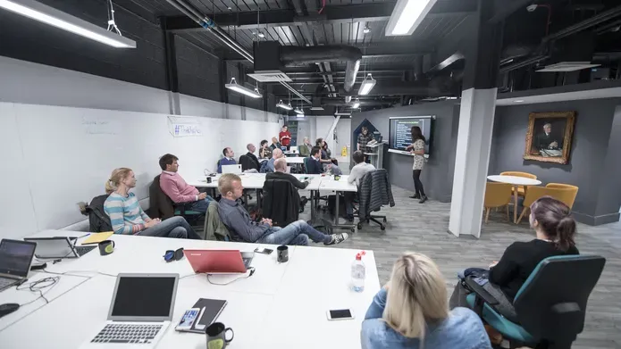 Students listen to a presentation in a room with coworking desks