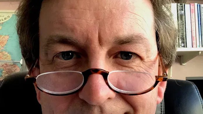 Bespectacled man smiling in front of bookshelves