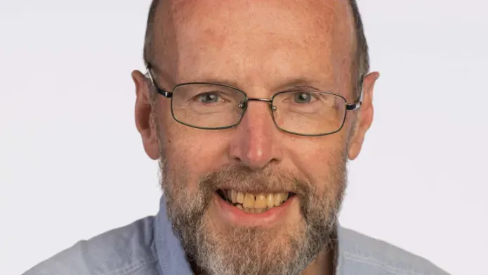 head shot of man wearing light blue shirt and thin glasses