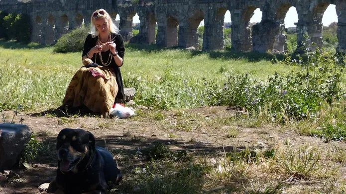 Fiona McHugh sitting in a field with an old acquaduct in the background and a dog at her feet