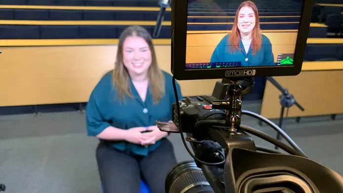 Cara sat behind a film camera talking