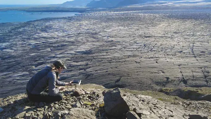 Dr Kieran Baxter observes some technical equipment in front of an expansive landscape