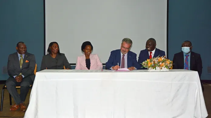 Principal Iain Gillespie sits at the centre of a table with a white table cloth. He is flanked by five representatives from Malawian universities as he signs an agreement.