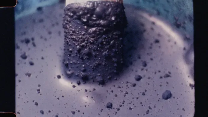 16mm film still picturing a close up of a paint brush in a powdery purple coloured tin of paint