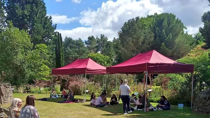 People sit under two red gazebos surrounded by trees.