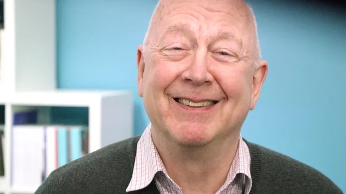 Older man looking directly at the camera and smiling, with a light blue background