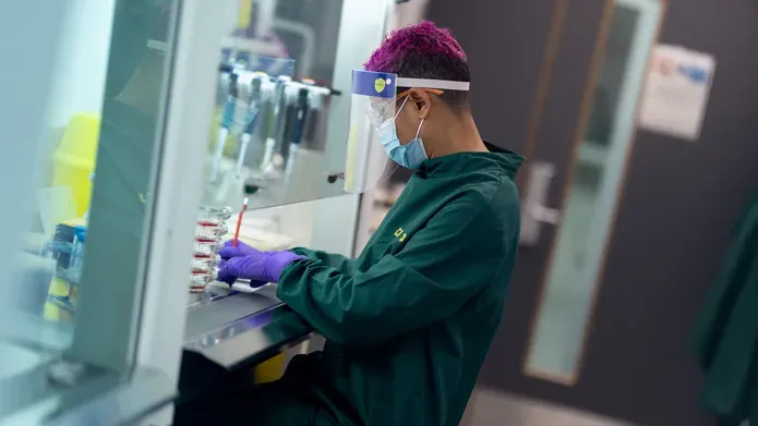 Person in green boiler suit facing left, working at scientific piece of equipment