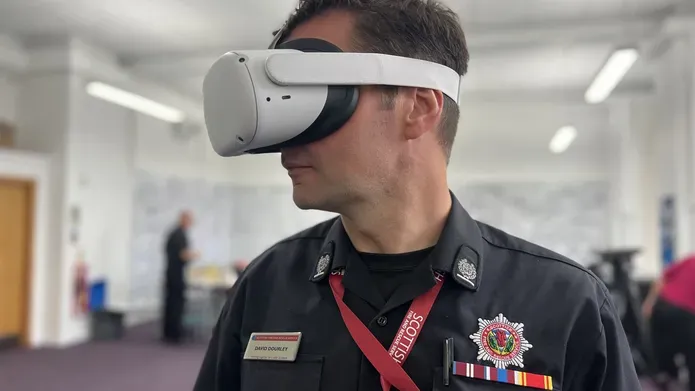 A man from the Scottish Fire and Rescue Service stands with a white VR headset mounted on his head