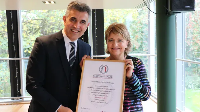 Wendy Alexander holding the framed University of Sanctuary award with a representative from City of Sanctuary