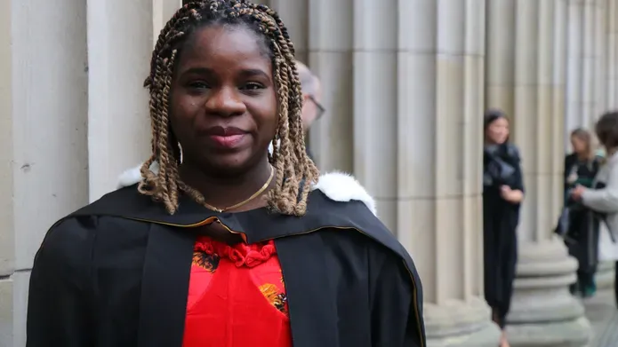 Martha, wearing graduation robes, stands outside the Caird Hall