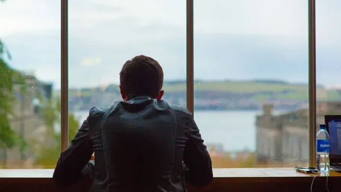 A student looks out of the window of DUSA, looking across the Tay to Fife.