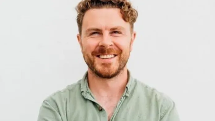 Alan is stood in front of a white background wearing a light green shirt. He's standing with his arms crossed, smiling into the camera.
