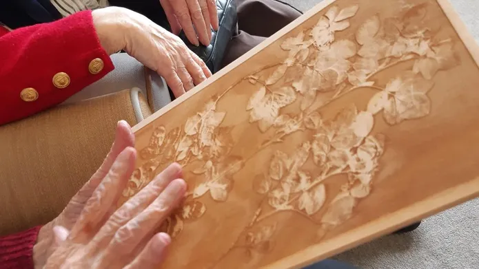 Photo of a seated person's hands holding a embossed wooden image. 