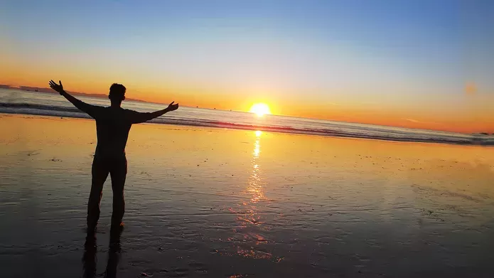 Person standing on beach at sunset with hands raised
