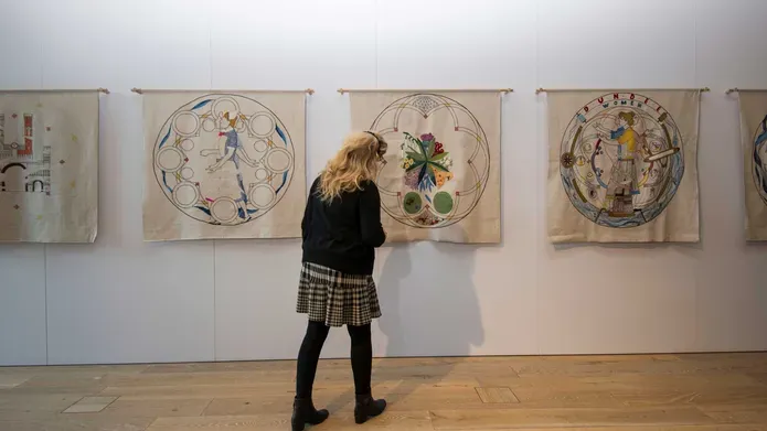 A female looks at a row of tapestries on the wall.