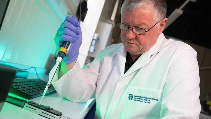 A male scientist in a lab coat and gloves pipetting a solution into a MinION, a pocket-sized device used sequence DNA & rNA.