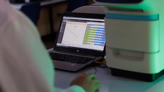Over the shoulder shot of a scientist examining a laptop running the StepOne PCR Software used to analyse DNA.