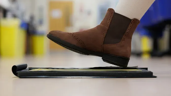 Side view of a woman’s boot held mid-air over an ink pad which is used to record footwear mark forensic evidence.