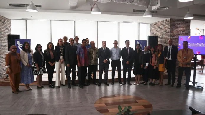 Mr Ivan McKee and stands with a group of people, in front of large windows.