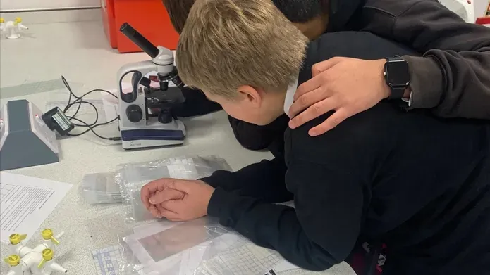 Photograph of S1 students at Baldragon Academy huddled together inspecting the fibres collected from their jumpers.