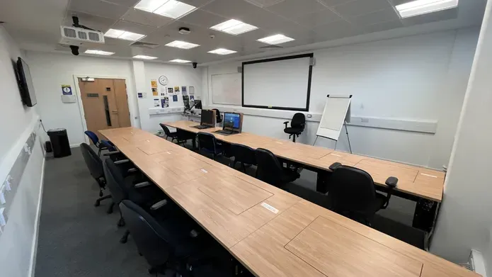 Dalhosuie 1LG02 showing two rows of desks and chairs. PCs are set inside the tables.  with a white screen on the wall