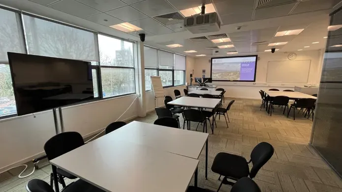 Dalhousie 1G10 - a room with several desks pushed together to form a square table with surrounding chairs and a tv screen and white screen at the far end