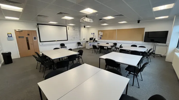Dalhousie 1S05 - four sets of square tables surrounded by chairs with a tv screen in the corner and a white screen at the front of the room
