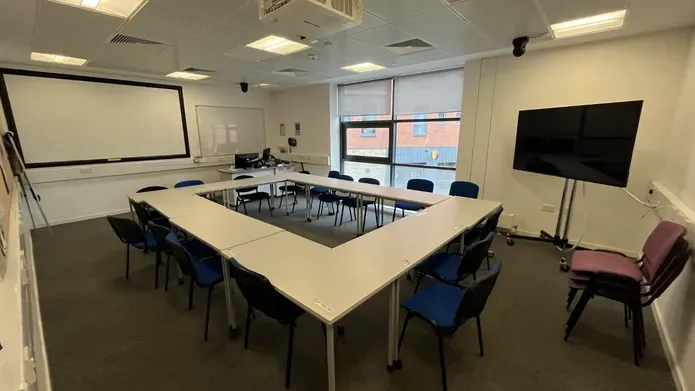 Dalhousie 2F02 - tables set in an oblong with chairs. A mobile tv screen and a white screen on the wall