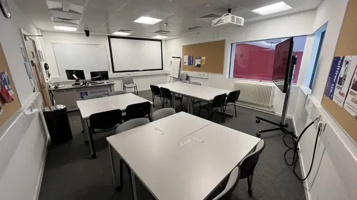 Dalhousie 2S11 - three sets of square tables with chairs, a mobile flat screen tv on the floor and a white screen on the far wall