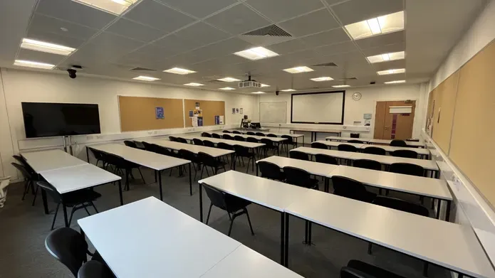 Dalhousie 2S13 - rows of tables and chairs with a white screen at the front of the room. A flat screen tv on a mobile stand on the floor 