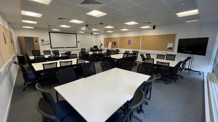 Dalhousie 2S14 - several tables set in squares with chairs. A mobile tv screen on the floor and white screen at front of room