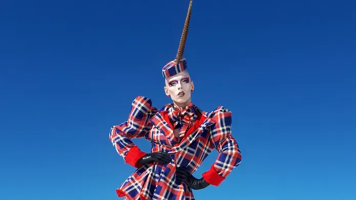 A model standing on top of a steep mountain with snow in a bright red and blue tartan suit