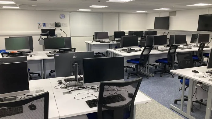 IT Suite in Tower Basement, Suite E showing several desks in a row with computer screens, keyboards and mouse