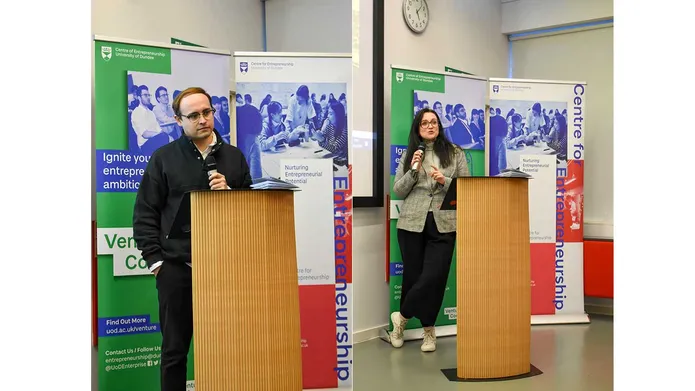 A male and female stand at a podium, talking to the room.